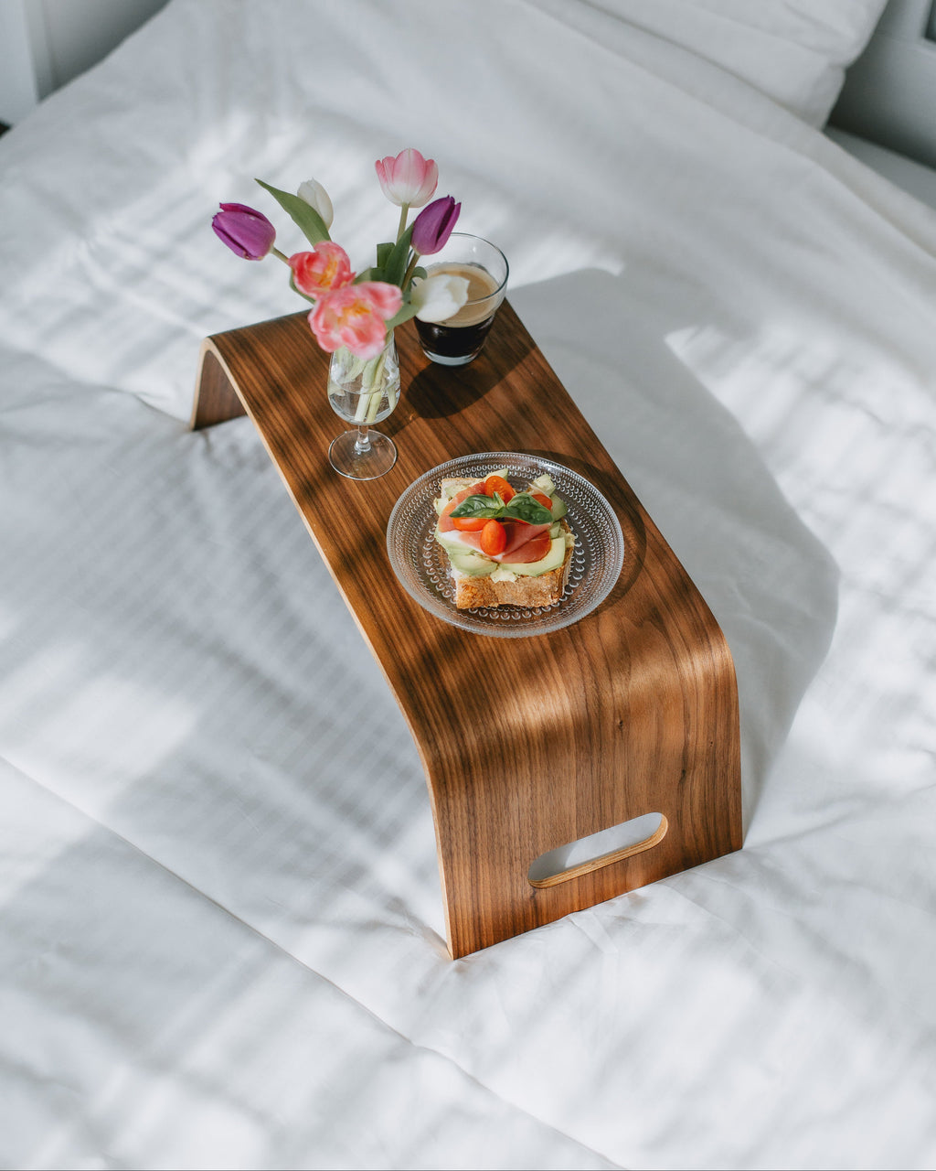 Wooden lap desk on a bed with a plate of food, coffee, and flowers.