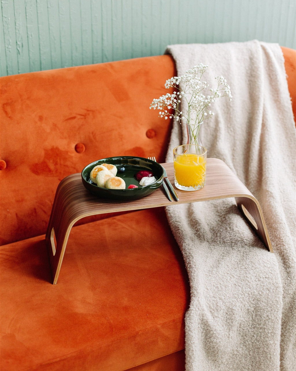 Orange sofa with a wooden side table holding a plate of food and a glass of orange juice, against a light green wall.