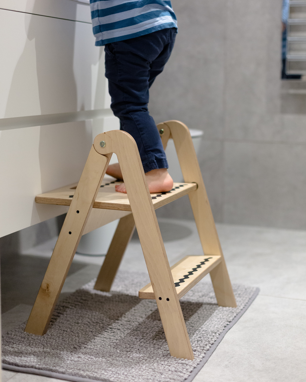 Child standing on a wooden step stool in a bathroom.