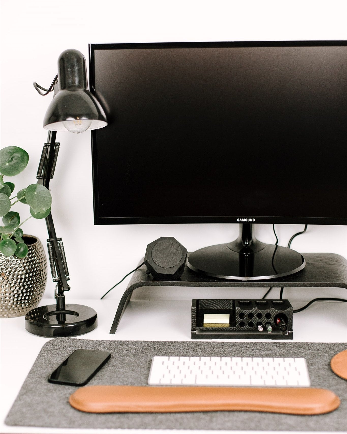 Modern office desk setup with computer monitor, lamp, magsafe charger and keyboard on a white surface.