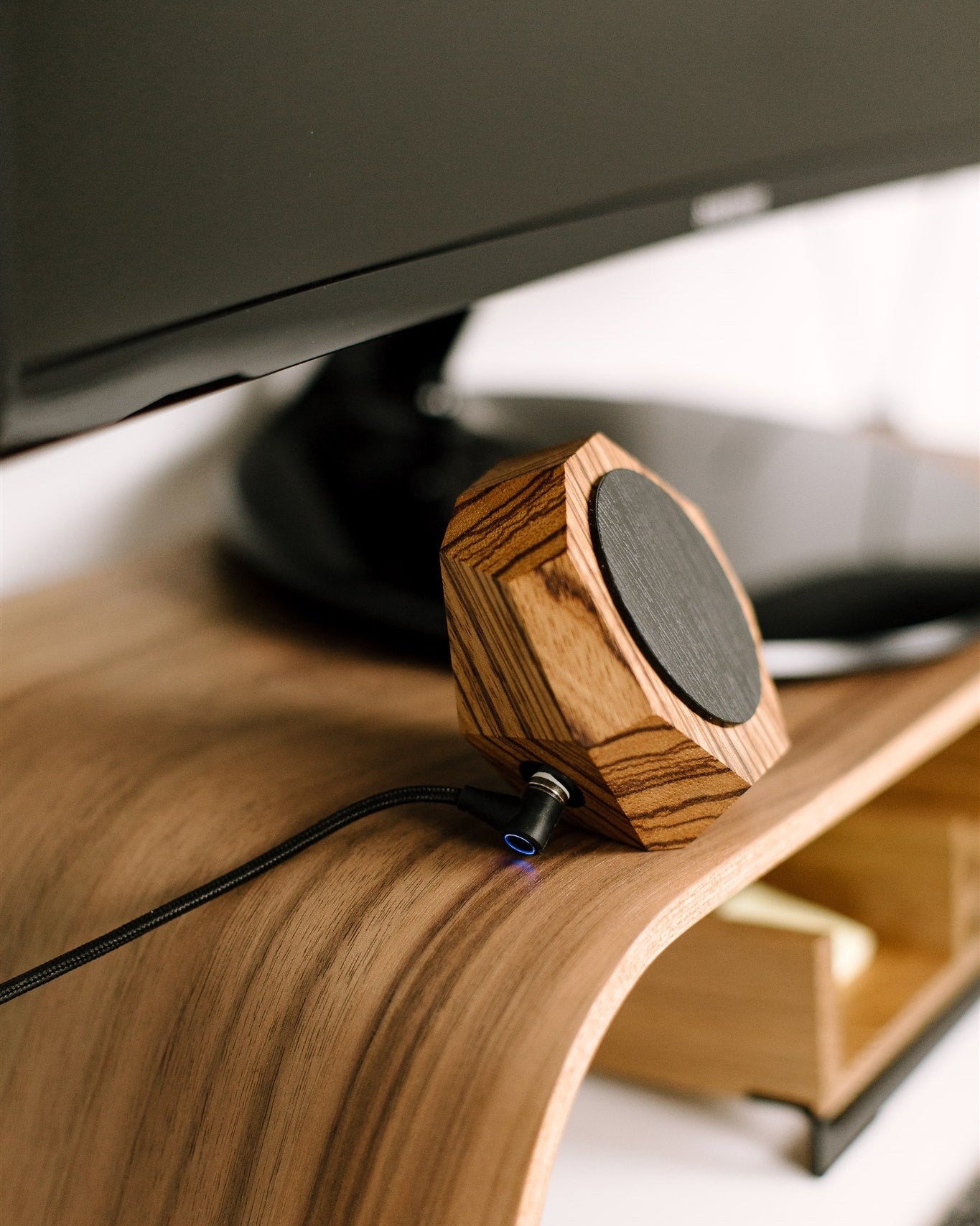 Wooden zebrano magsafe phone charger on a desk with a computer monitor in the background