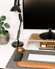 Modern office desk setup with computer monitor, lamp, keyboard, american walnut magsafe phone charger and decorative items.