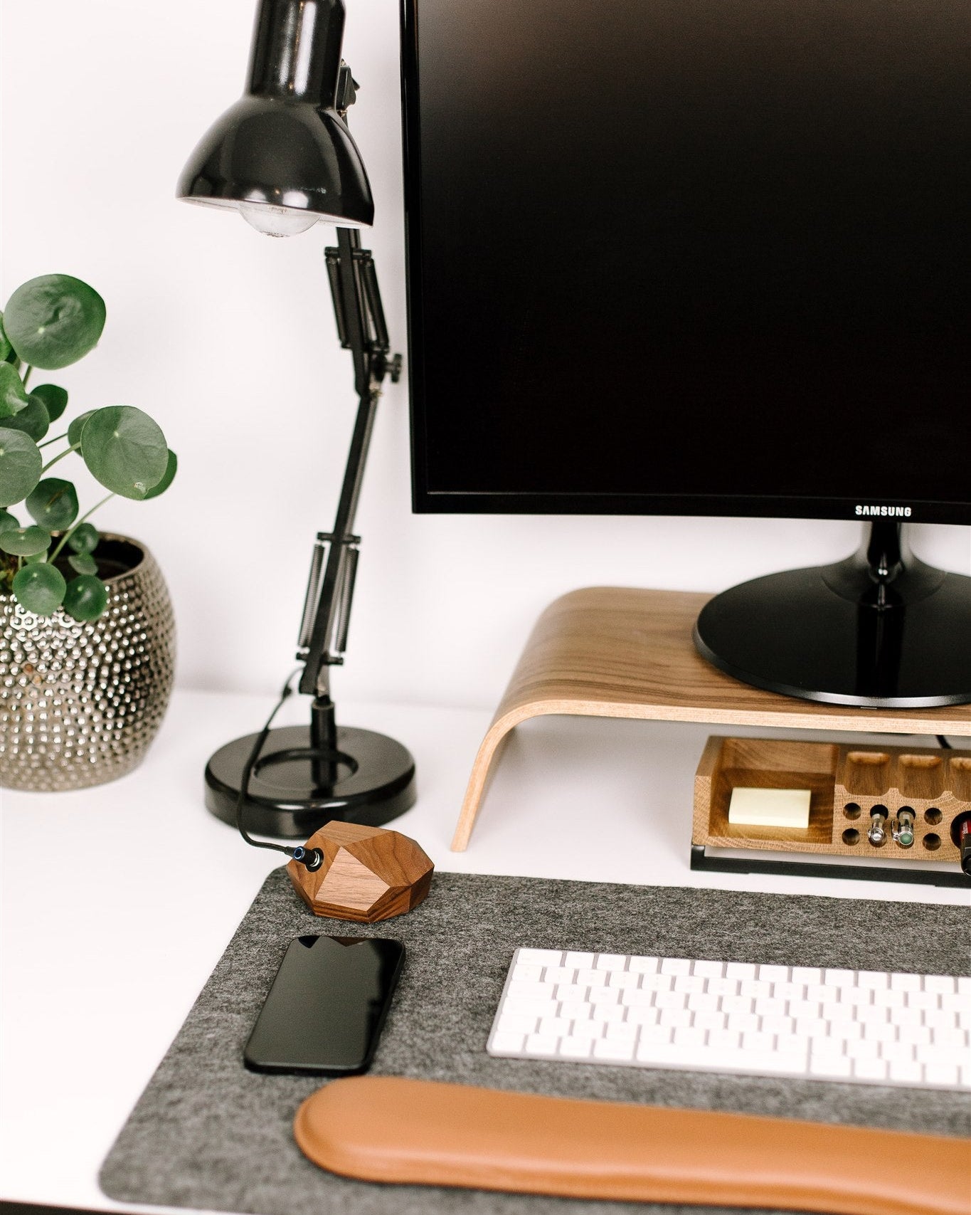 Modern office desk setup with computer monitor, lamp, keyboard, american walnut magsafe phone charger and decorative items.