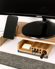 Wooden desk organizer with Samsung monitor, phone, and stationery items on a white surface.