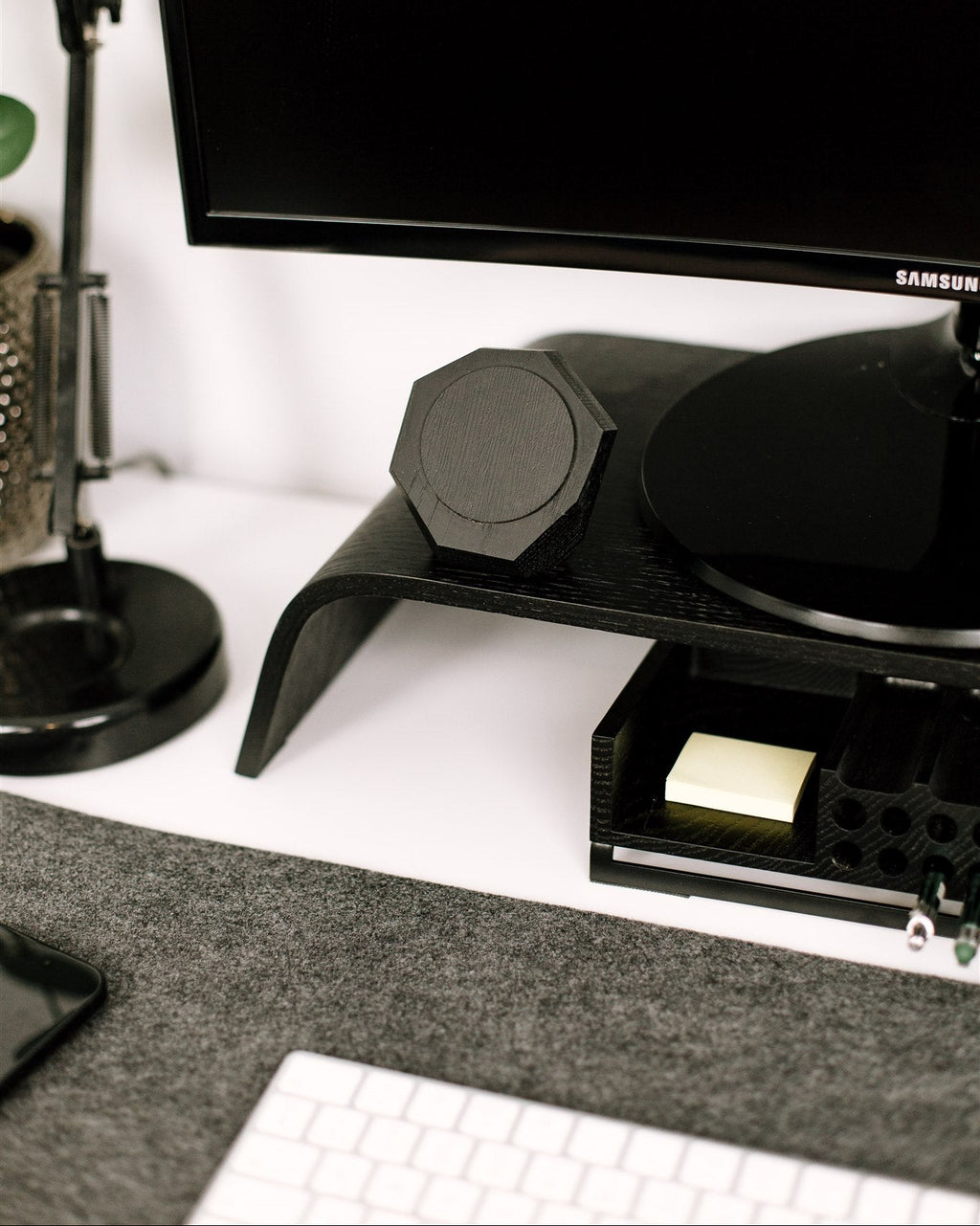 Samsung monitor on a stand with a pen holder and notepad on a desk and magsafe phone charger