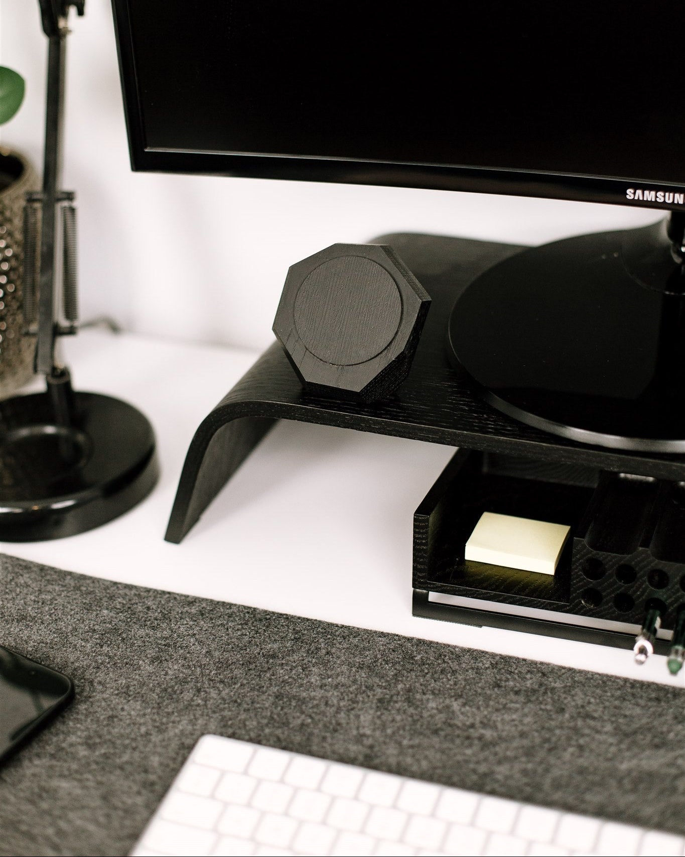 Samsung monitor on a stand with a pen holder and notepad on a desk and magsafe phone charger