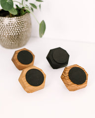 Hexagonal wooden magsafe chargers with black centers on a white surface with a plant in the background.