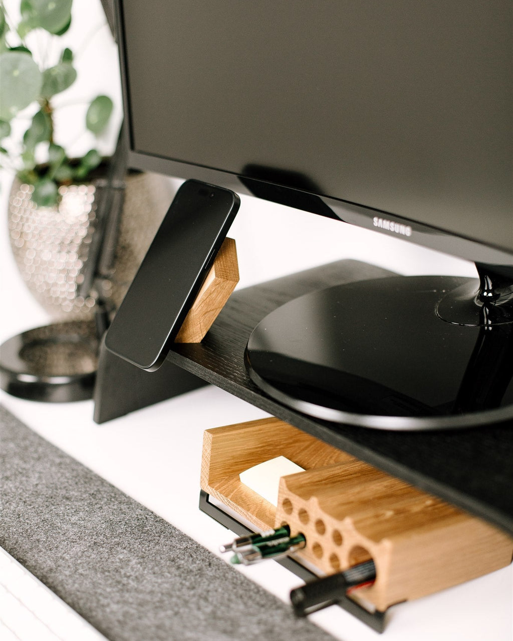 Black Samsung monitor on a wooden stand with a plant in the background